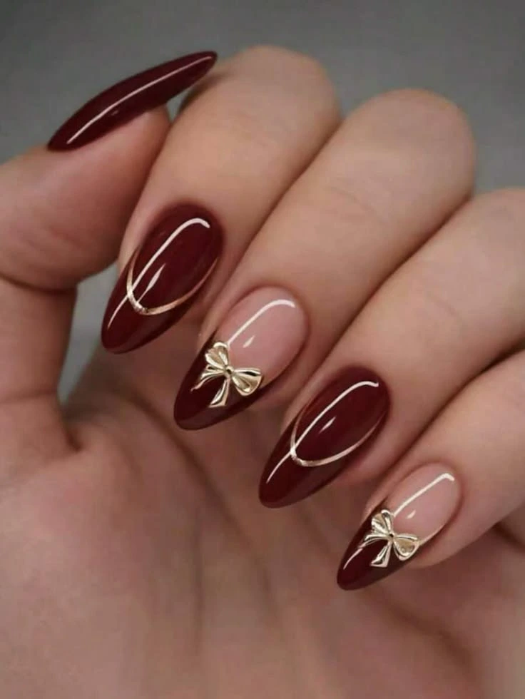 Press-on nails with burgundy almond shape and gold bow nail art at Mark Salon, Hoshiarpur